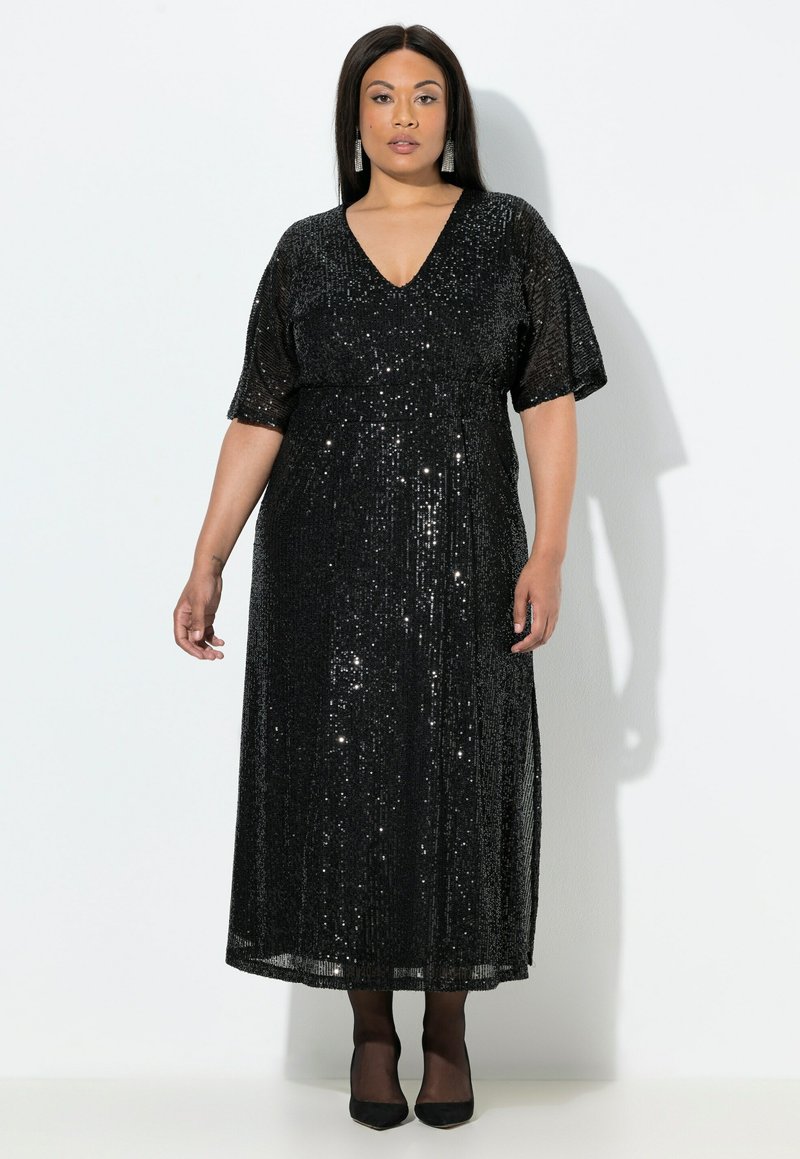 Černé maxi šaty s flitry, hlubokým výstřihem do V a krátkými rukávy. Šaty mají splývavý střih a hladkou texturu, nosí se s černými podpatky.