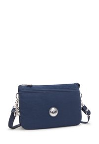 Mörkblå crossbody-väska gjord av slitstarkt material med en silverfärgad logotypdetalj, dragkedjestängning och justerbar rem. Kompakt rektangulär form.