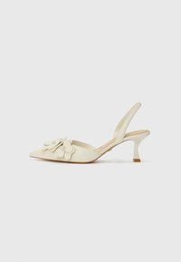 Talons slingbacks de couleur crème avec un bout pointu, des embellissements floraux sur le devant et un talon fin et courbé.