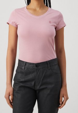 Vaaleanpunainen, lyhythihainen t-paita pyöreällä pääntiellä, yhdistettynä mustiin housuihin, joissa on sileä pinta ja minimaalinen brändäys rinnassa.