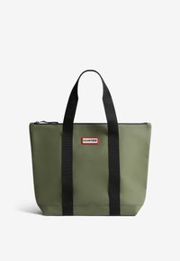 Green waterproof tote bag with black straps, zip closure, and a red and white logo patch on the front. Smooth texture, rectangular shape.
