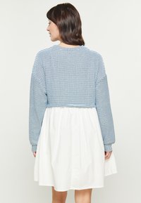 Pulover scurt, cu dungi albastre și mâneci lungi, asortat cu o fustă albă, vaporoasă. Prezintă mansete striate și un guler rotund. Textură moale cu un design stratificat.