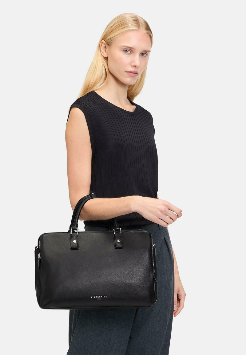 Sac à main en cuir noir avec une forme structurée, poignées supérieures doubles, fermeture éclair et accents en métal argenté. Surface texturée.