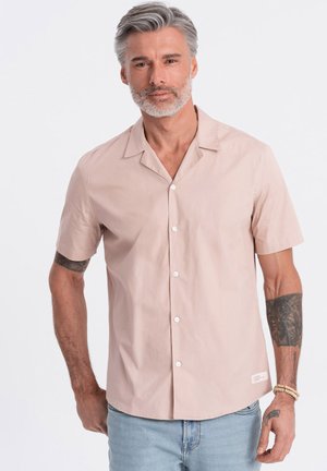 Camisa de botones de manga corta de color rosa claro hecha de algodón suave, con un cuello con muesca y botones blancos, combinada con jeans de color azul claro.