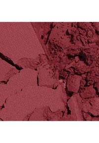 Poudre de maquillage rouge foncé écrasée, composée de sections texturées et libres, remplissant le cadre sur fond blanc.