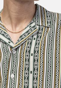 Short-sleeve shirt in green with vertical stripes, featuring geometric patterns in white, cream, and yellow; includes a collar and button front.