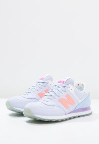 Baskets New Balance 574 en bleu clair et pêche, avec une tige en mesh et synthétique, un col rembourré et une semelle translucide.