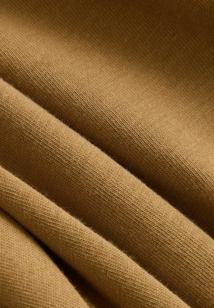 Pehmeä, teksturoitu kangas lämpimässä sinapin värissä, joka esittelee hienoja neulekuvioita hienovaraisilla sävyeroilla ja sileällä laskeutumisella.