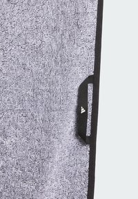 Szary, teksturowany ręcznik z czarną lamówką oraz małą czarną metką z białym logo. Powierzchnia prezentuje pętelkową teksturę.