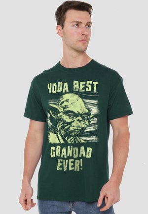 Grünes Baumwoll-T-Shirt mit Yoda-Grafik und dem Text "YODA BESTE GROßVATER ÜBERHAUPT!" in Gelb. Kurzärmlig, Rundhalsausschnitt.