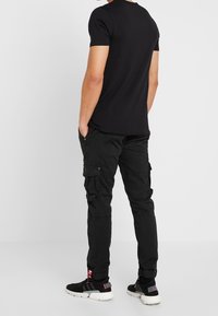 Svart kortärmad t-shirt ihop med svarta cargo-byxor. Byxorna har flera fickor och elastiska muddar. Svarta sneakers fulländar looken.