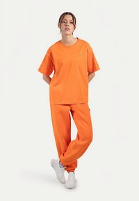 Orange bomullst-shirt med korta ärmar och lös passform, kombinerad med matchande orange sweatpants med elastisk dragsko vid anklarna.