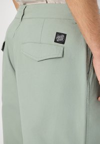Lichtgroene broek van zachte stof, met een achterzak voorzien van een zwart logo-label en een eenvoudig, functioneel ontwerp.