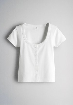 Krátky biely rebrovaný crop top s výstrihom do lodi a malými prednými gombíkmi na svetlom pozadí.