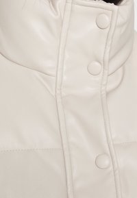 Cream-colored faux leather jacket with a high collar, prominent button closures, and subtle stitching details. Smooth texture, modern design.