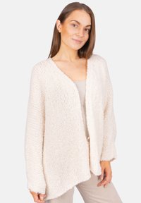 Strickjacke in Creme mit strukturiertem Oberflächen, offener Vorderseite und lockeren Ärmeln, die sich durch eine entspannte Passform und natürlichen Fall auszeichnet.