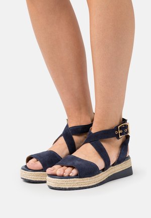 Marineblauwe suède sleehak sandalen met gekruiste bandjes, verstelbare gesp en espadrille-achtige touwen middenzool. Open teen ontwerp.