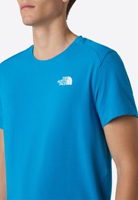 Modrá polokošile s krátkým rukávem vyrobená z lehké tkaniny. Má kulatý výstřih a bílé logo na levé části hrudi.