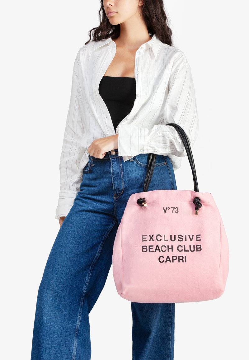 Roze canvas draagtas met zwarte trekkoorden en tekst "EXCLUSIVE BEACH CLUB CAPRI." Zwarte leren handvatten. Casual ontwerp.