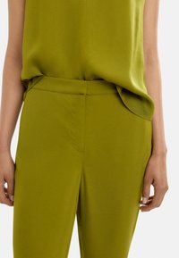 Jasnozielone, lekkie spodnie o gładkiej fakturze, z płaskim przodem, bocznymi kieszeniami i dopasowanym krojem.