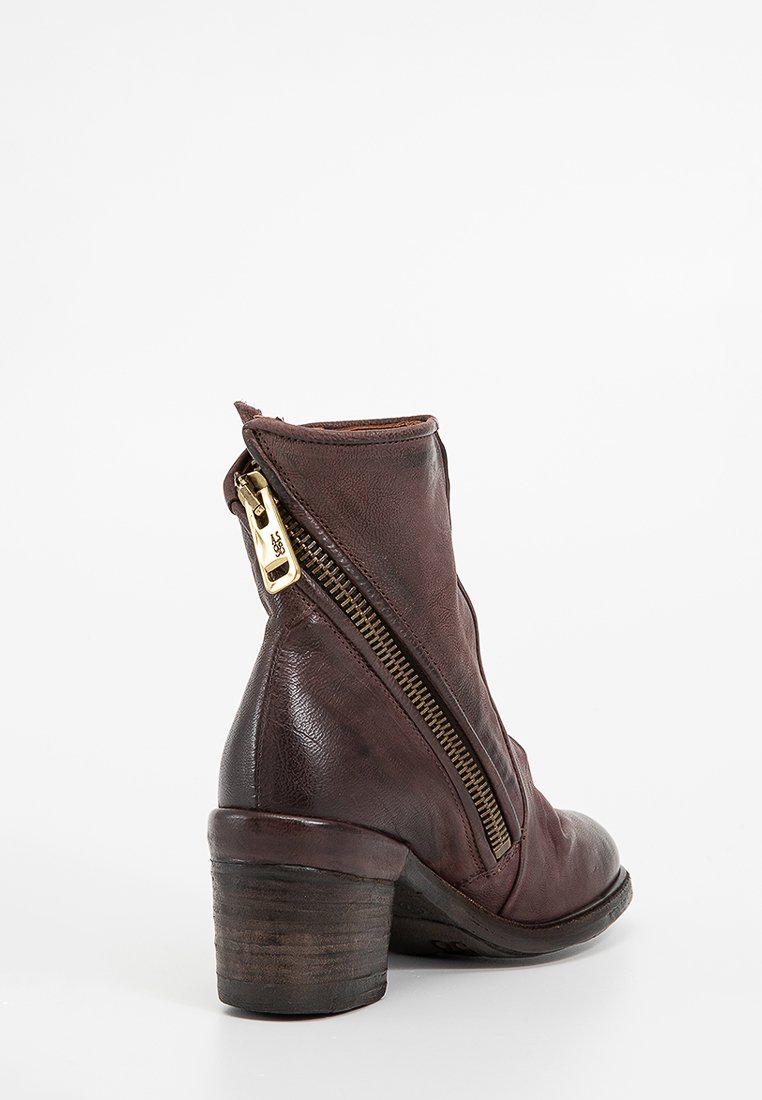 Smeđe kožne gležnjače sa malo šiljastim prstima, zlatnim zatvaračem sa strane i drvenim potplatom. Glatka tekstura.