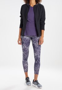 Veste zippée noire, t-shirt violet et leggings violets à motifs, associés à des chaussures de sport grises, conçus pour les vêtements de sport.
