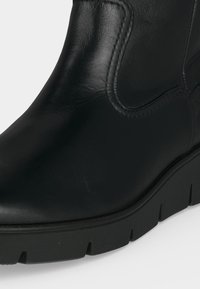 Bottine noire en cuir avec panneau latéral élastique et semelle épaisse en caoutchouc avec un profil profond pour une bonne adhérence.
