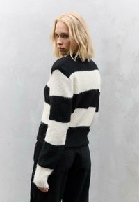 Un pull à rayures noires et blanches avec une texture douce, un ourlet côtelé et de longues manches. Le modèle qui le porte fait face à l'arrière de l'appareil photo.