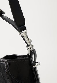 Cinghia di pelle lucida nera con chiusura in metallo argentato e attacco ad anello su una borsa a mano con finitura lucida e texture.