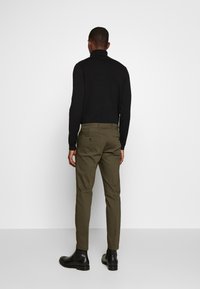 Maglione nero a collo alto, pantaloni verde oliva e stivali neri alla caviglia. I pantaloni presentano tasche posteriori e una vestibilità slim.