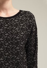 Top nero in maglia con un motivo in pizzo testurizzato. Presenta un collo rotondo e maniche lunghe, mettendo in risalto il design intricato in tutto il capo.