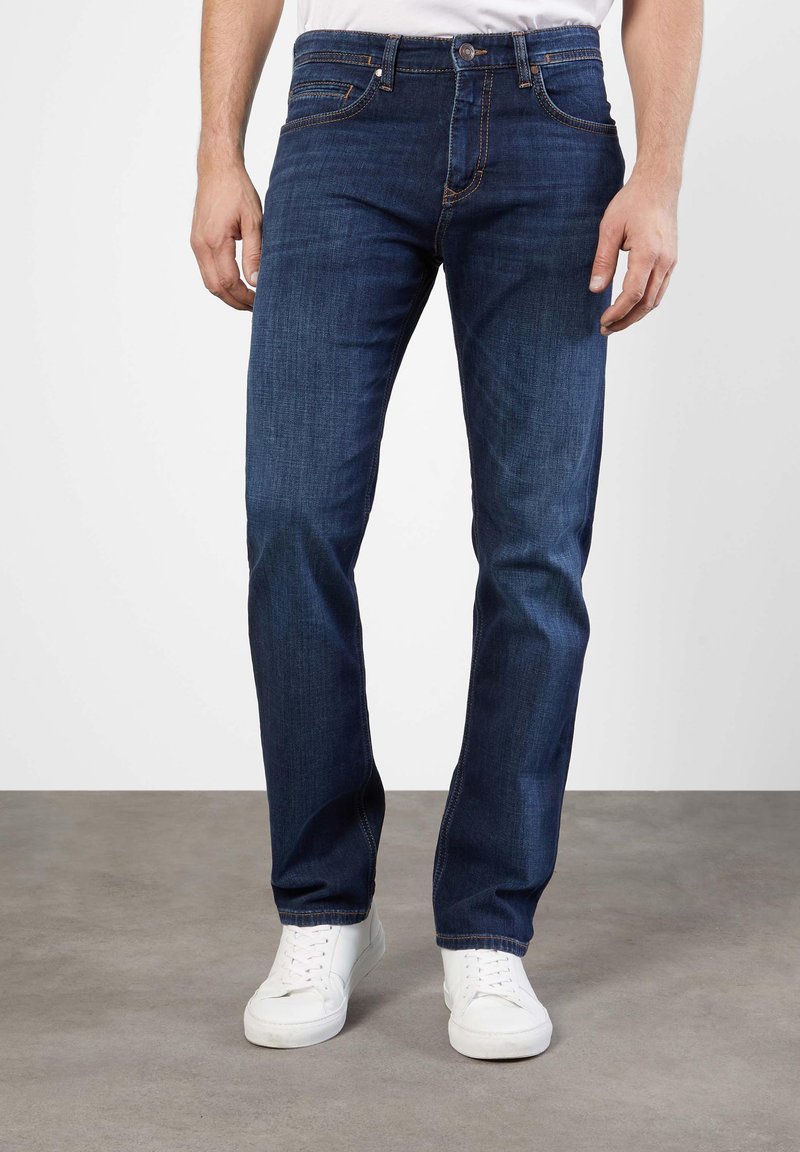 Dark blue denim jeans with a straight leg design, five pockets, and stitching accents. Paired with white sneakers.