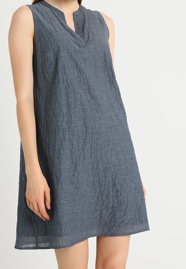Robe sans manches texturée gris foncé longueur genou avec une petite fente en V portée par une personne sur un fond clair uni.