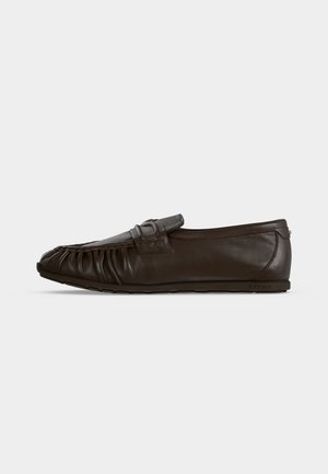 Σκούρο καφέ δερμάτινο loafer τύπου slip-on με ρυτιδωτές λεπτομέρειες στο μπροστινό μέρος και επίπεδη καουτσούκ σόλα σε μονόχρωμο φόντο.