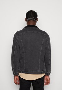 Mörkgrå denimjacka med en svart fårskinnskrage, med avslappnad passform och knapprad vid ärm- och nederkant.