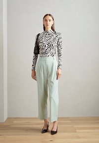 Zebra vzorec v črno-beli barvi s dolgimi rokavi v kombinaciji z metino zelenimi hlačami z visokim pasom in črnimi čevlji s koničastim nosom, ki so dopolnjeni z majhno torbico.