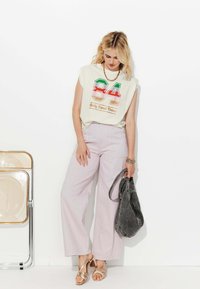 Haut sans manches blanc avec un graphique coloré "84", pantalon large rayé rose clair, sandales métalliques et un sac à main gris.