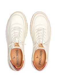 Zapatos de piel blanca con forma redondeada, cordones blancos y un suave forro interior marrón. Presentan un sutil acento rojo en el talón.