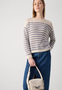 Gestreepte gebreide trui in crème en blauw, ronde halslijn, lange mouwen, met een textuurafwerking. In combinatie met een spijkerrok en een beige tas.