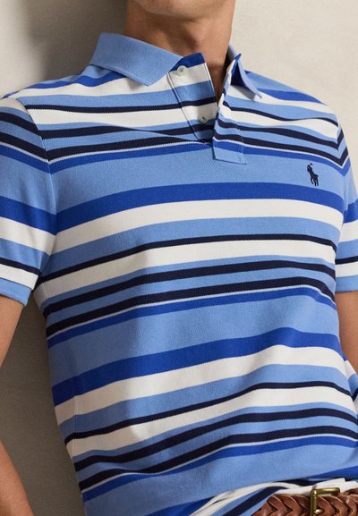 Homme portant un polo à rayures horizontales bleu, blanc et marine avec col et patte de boutonnage, associé à une ceinture tressée marron.