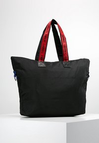 Borsa tote nera realizzata in materiale resistente, con spallacci rossi con logo, dettagli blu, chiusura con zip e forma strutturata.