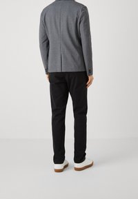 Blazer grigio con texture, dotato di uno spacco singolo sul retro, abbinato a pantaloni neri e sneakers bianche con suole in gomma marrone.