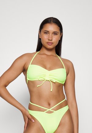 Conjunto de biquíni verde néon com parte superior tipo bandeau com franzidos e detalhes de nó, e parte inferior alta com tiras cruzadas. Tecido suave e elástico.