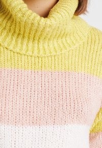 Sweter z golfem, dziany w żółte, różowe i białe paski. Posiada ryflowaną teksturę i gruby włókno dla ciepła.