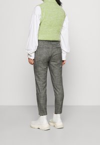 Grön stickad ärmlös topp, vit långärmad skjorta, grå rutiga byxor och vita ankelstövlar, sedd bakifrån.