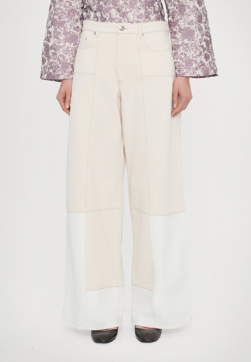 Brede broek in lichtbeige en wit, gemaakt van een getextureerde stof met zichtbare stiknaden. Voorzien van vier zakken en een knoopsluiting aan de voorkant.