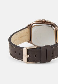 Pruun nahast kellarihm roosakuldsest pandlast ja nähtava Tommy Hilfiger logo rihma sees.