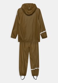 Giacca impermeabile marrone con cappuccio e pantaloni abbinati. Presenta polsini elasticizzati e dettagli riflettenti bianchi sulle maniche e sui pantaloni.