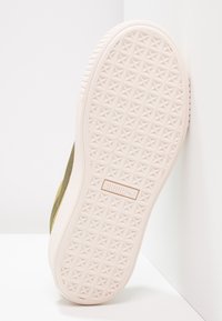 Puma tenisky s texturovanou bílou gumovou podešví, kruhovým vzorem hvězdy; svrchní část v olivově zelené barvě se semišovým povrchem. Plochej design podpatku, minimální branding.