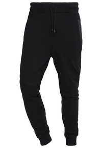 Czarne spodnie dresowe z polarowego materiału z sznurkiem w pasie, żeberkowymi wykończeniami przy kieszeniach, zwężanymi nogawkami oraz elastycznymi mankietami przy kostkach.